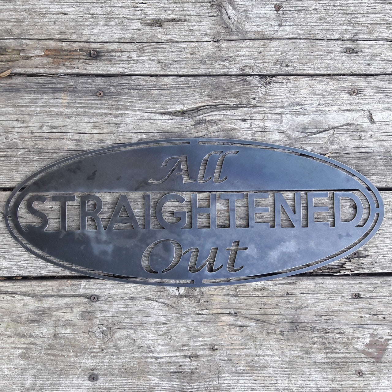 This metal sign is an oval, it has three lines of text. The sign reads, "All Straightened Out"