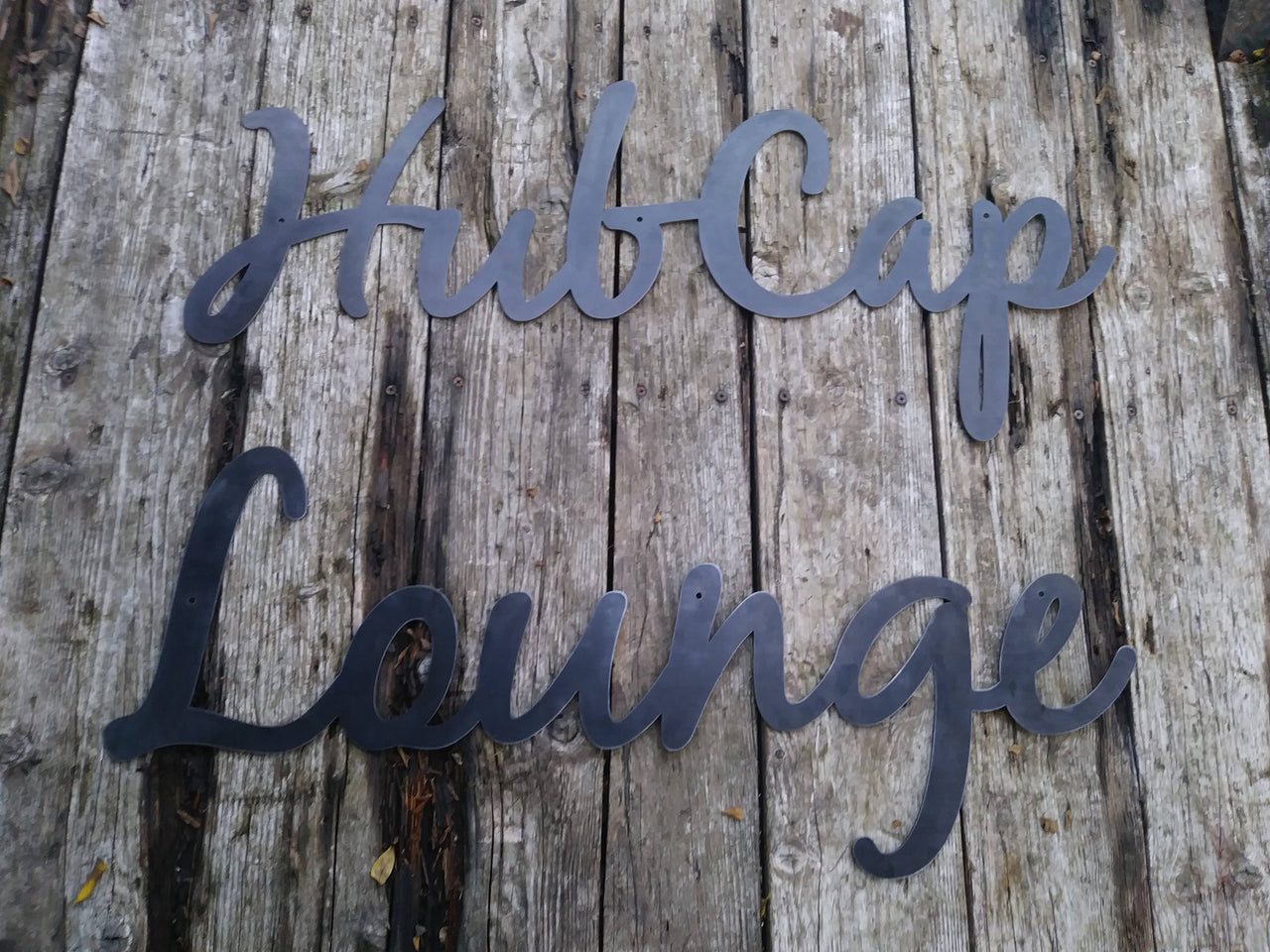 This is a custom metal cursive sign that is powder coated black and reads' "Hubcap Lounge".